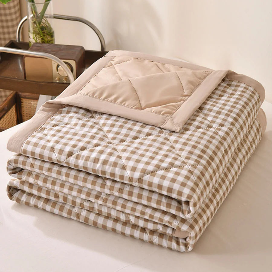 Beige and white gingham quilted comforter folded on a bed with a beige border