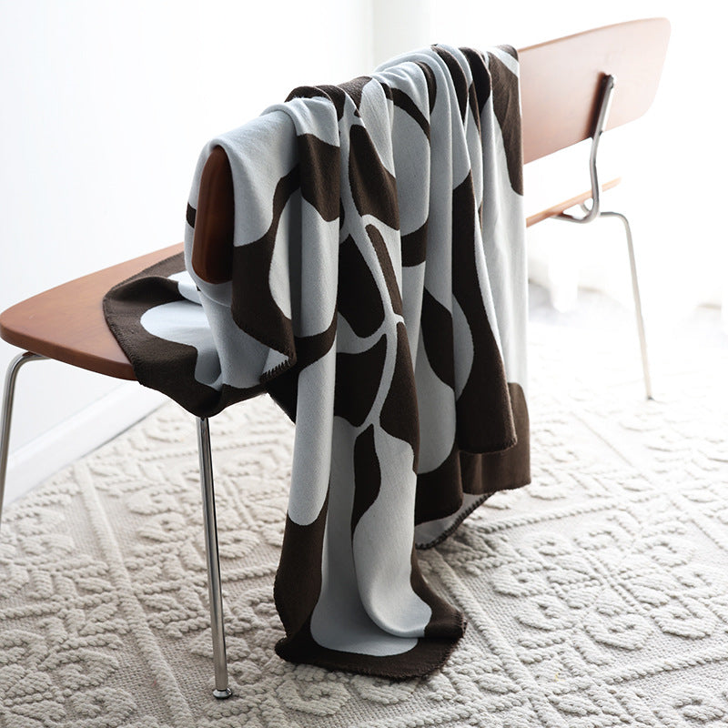 Mocha and grey abstract jacquard blanket draped over a wooden chair on a textured cream rug
