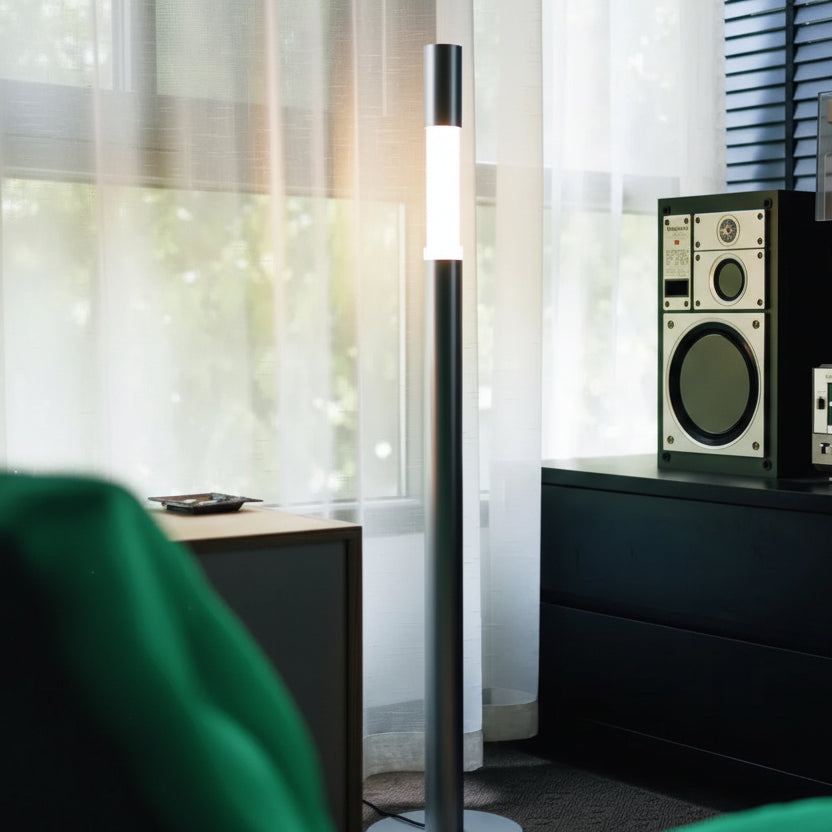 Minimalist Gun Black floor lamp styled in a modern living room next to a designer chair.