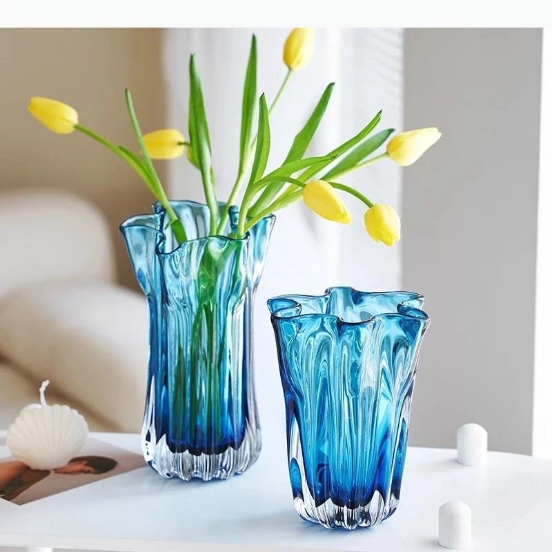 Two blue glass vases with yellow tulips on a white surface.