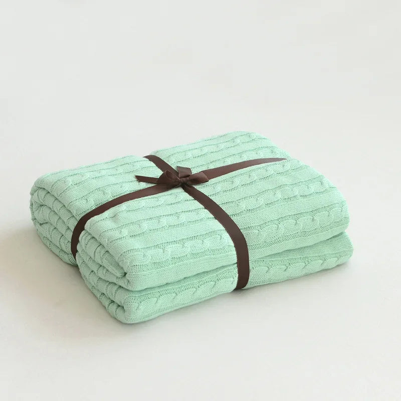 Folded mint green blanket tied with a brown ribbon on a light gray background