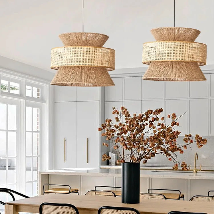 Two wicker pendant lights hanging above a dining table with a vase of dried flowers.