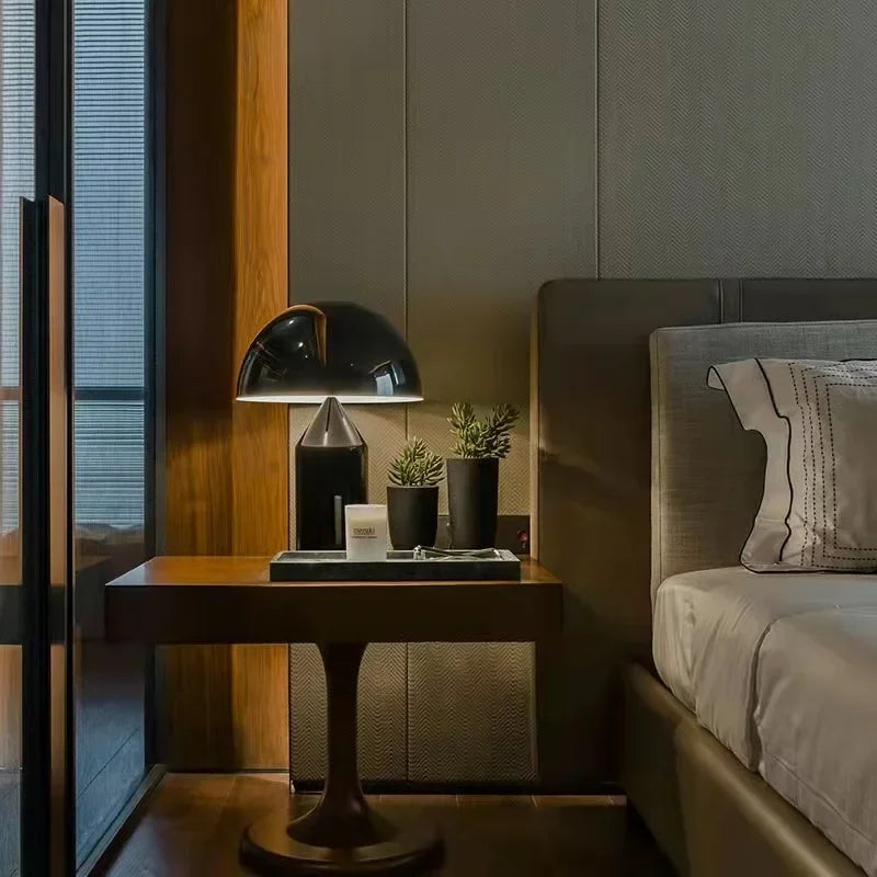 Modern bedroom with a bedside table, lamp, and plants.