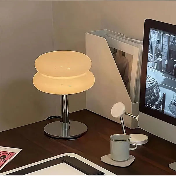 Modern desk setup with a warm glow table lamp, computer monitor, and mug on a wooden surface. 