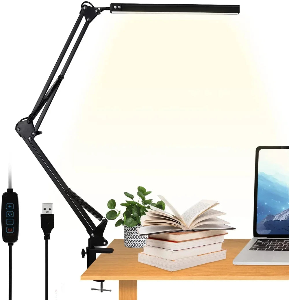 A adjustable black desk lamp on a table with books and a laptop