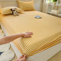A high-angle shot of a bed featuring a yellow and white mini-plaid gingham fitted sheet and matching pillowcase. A small plush dog toy sits on the pillow against a cream-colored headboard.