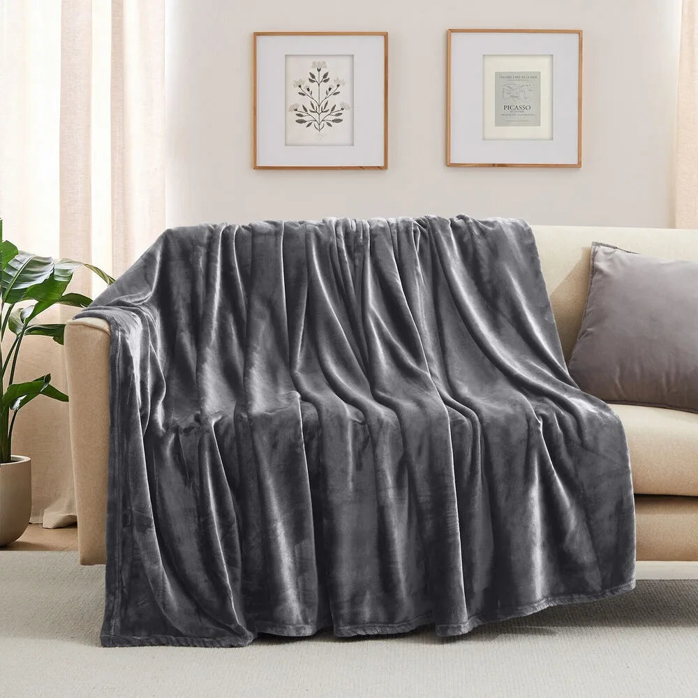 A grey blanket is draped over a beige sofa in a living room with framed pictures on the wall.