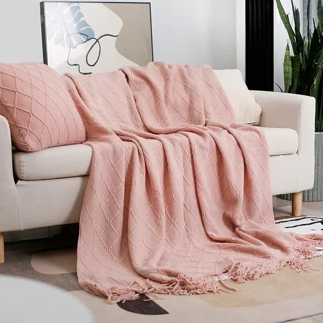 Dusty pink knit throw with a diamond texture and fringe styled over a cream sofa beside a matching cushion