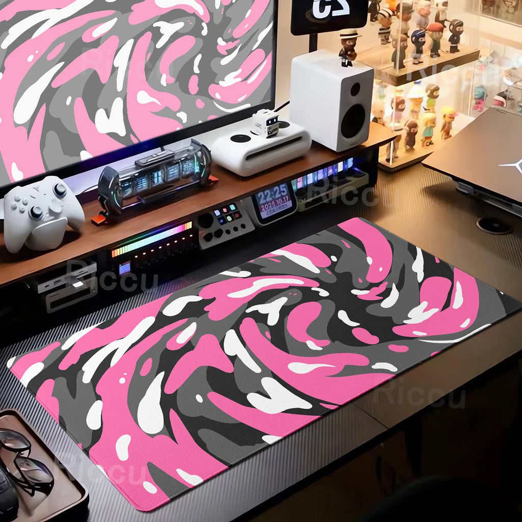 Desk setup with a pink and gray camouflage mouse pad, computer equipment, and a monitor displaying a pink and gray pattern.