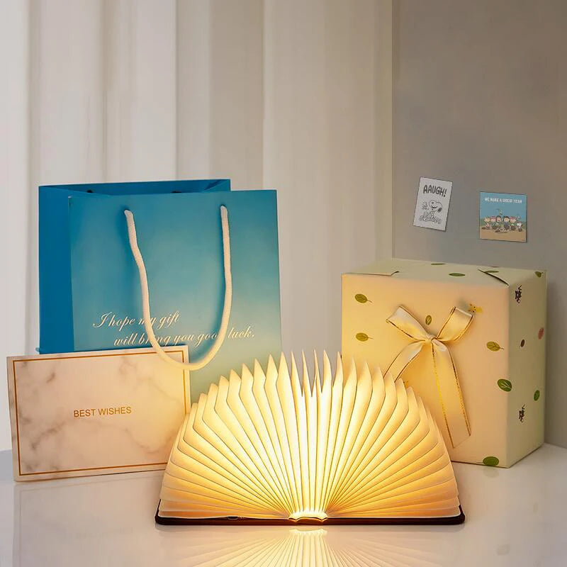 Book-shaped lamp with gift box, blue bag, and card on a white surface