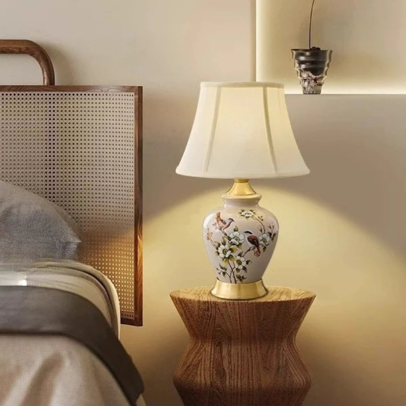 Decorative table lamp with floral design on a wooden side table in a bedroom setting.