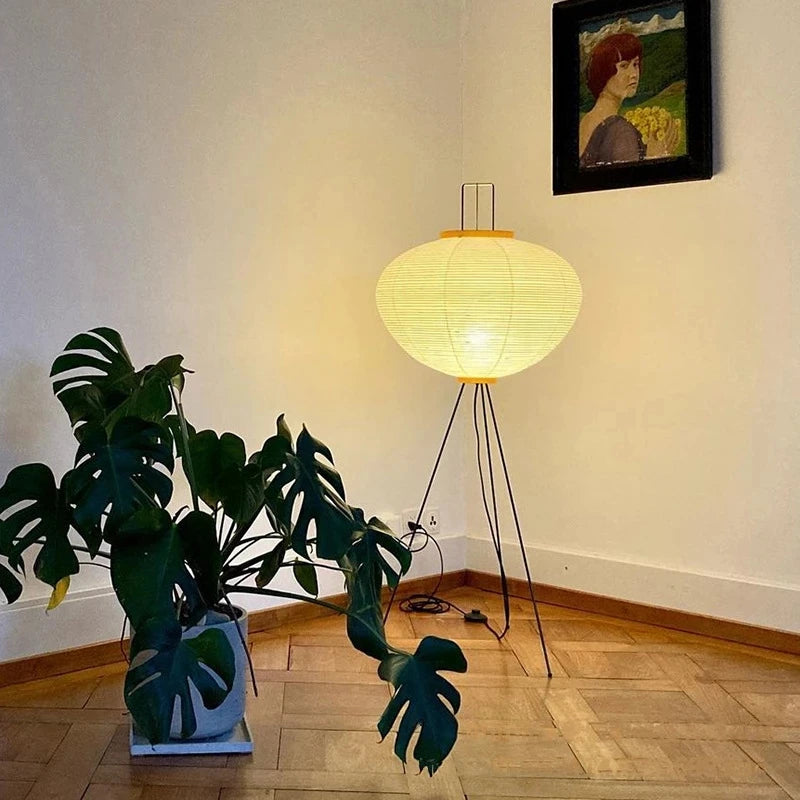 A Japanese floor lamp with a plant and a painting on the wall in a room.