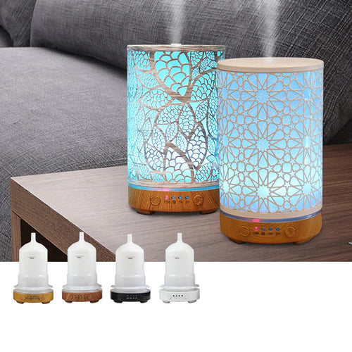 Two aroma humidifiers with decorative glass designs on a wooden table, with a gray sofa in the background.