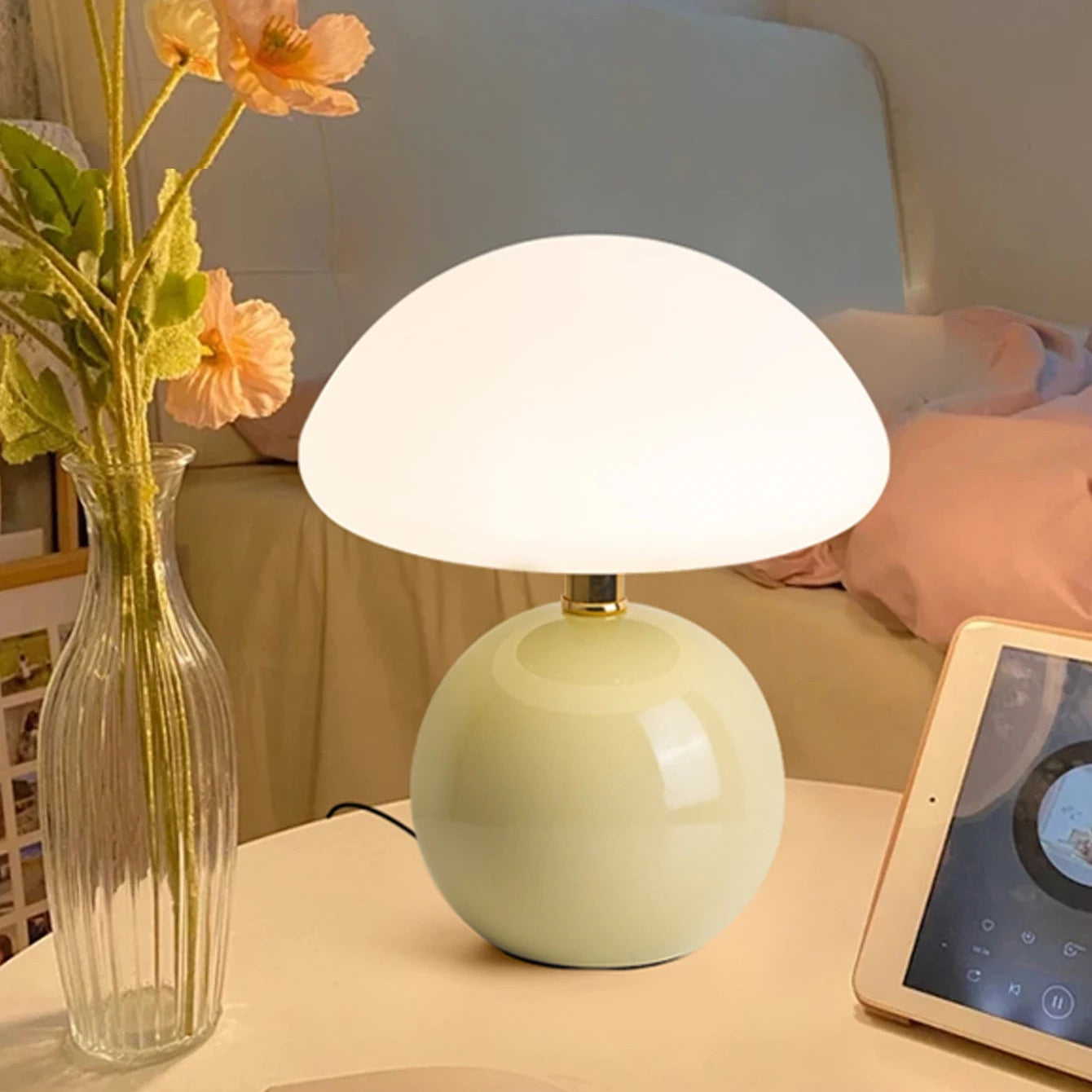 Light green table lamp on a surface with a tablet and vase in the background