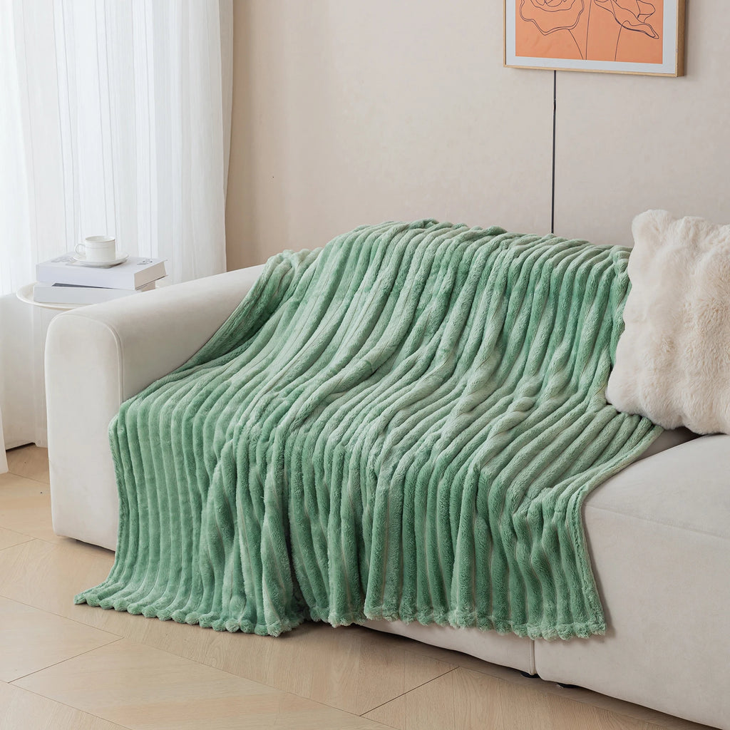 Green blanket draped over a white sofa in a living room setting.