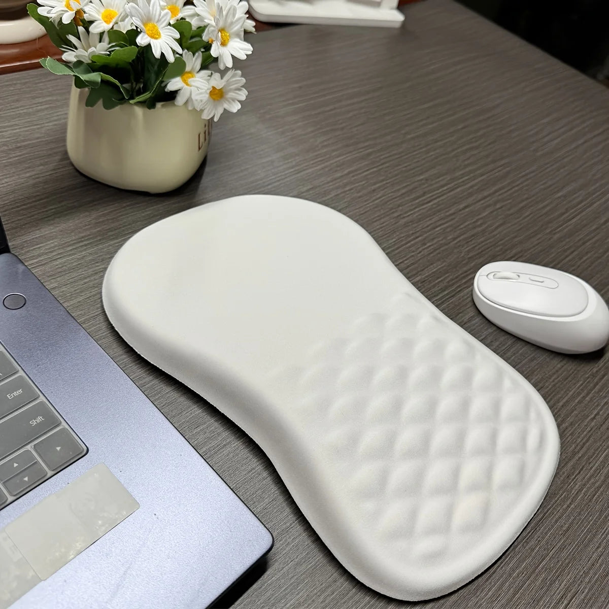 White wrist rest on a desk with a laptop, mouse, and flowers in the background