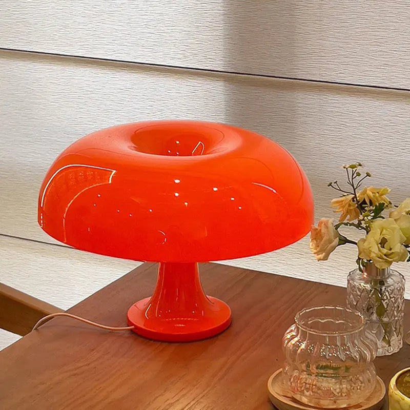 Orange mushroom shape table lamp on a wooden surface with a vase of flowers in the background