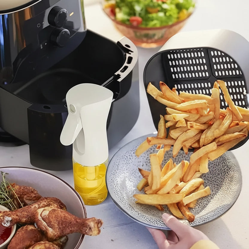 Air fryer with cooked french fries on a plate, surrounded by cooking accessories on a kitchen counter.