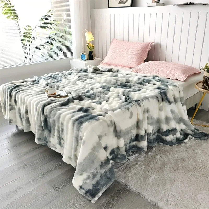A green and white tie-dye blanket on a bed with pink pillows in a bright room.
