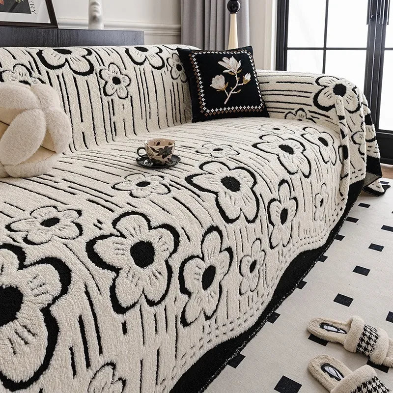 Cream and black floral-patterned sofa throw with bold contrast edging, neatly layered over a modern armchair sofa in a bright interior setting.