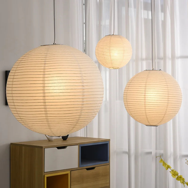 Three spherical Japanese rice paper lampshades hang in a room with a wooden cabinet and curtains.