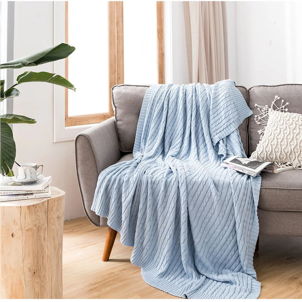 Light blue textured blanket draped over a gray sofa in a cosy living room.