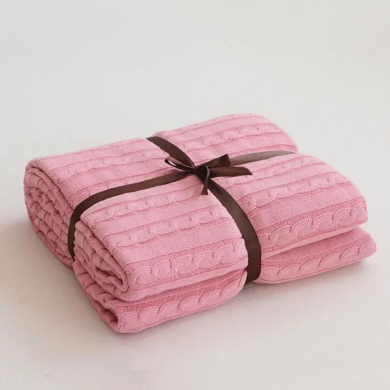 Folded pink blanket with a brown ribbon on a light gray background