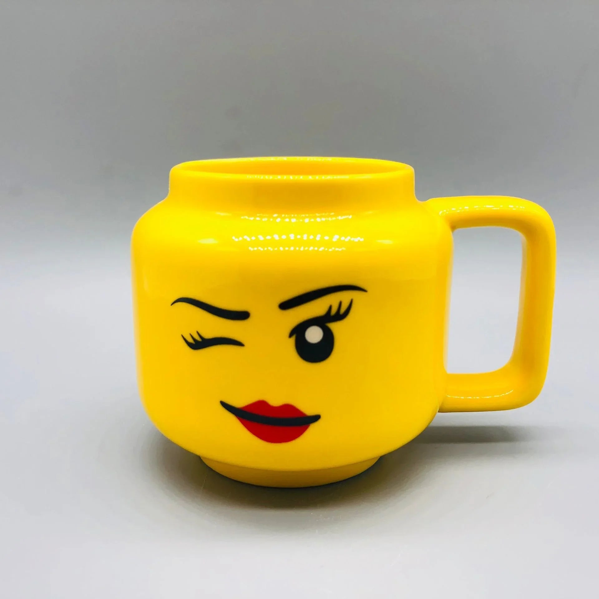 Yellow mug designed with a woman winking face on a grey background