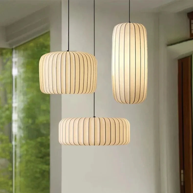 Three pendant lights hanging above a dining table with a view of greenery outside.