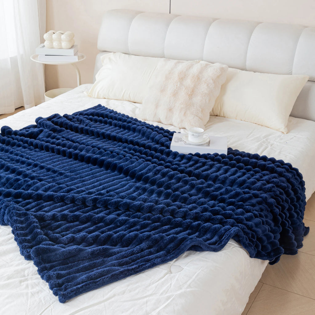 Navy blue textured blanket on a white bed with pillows and a headboard.