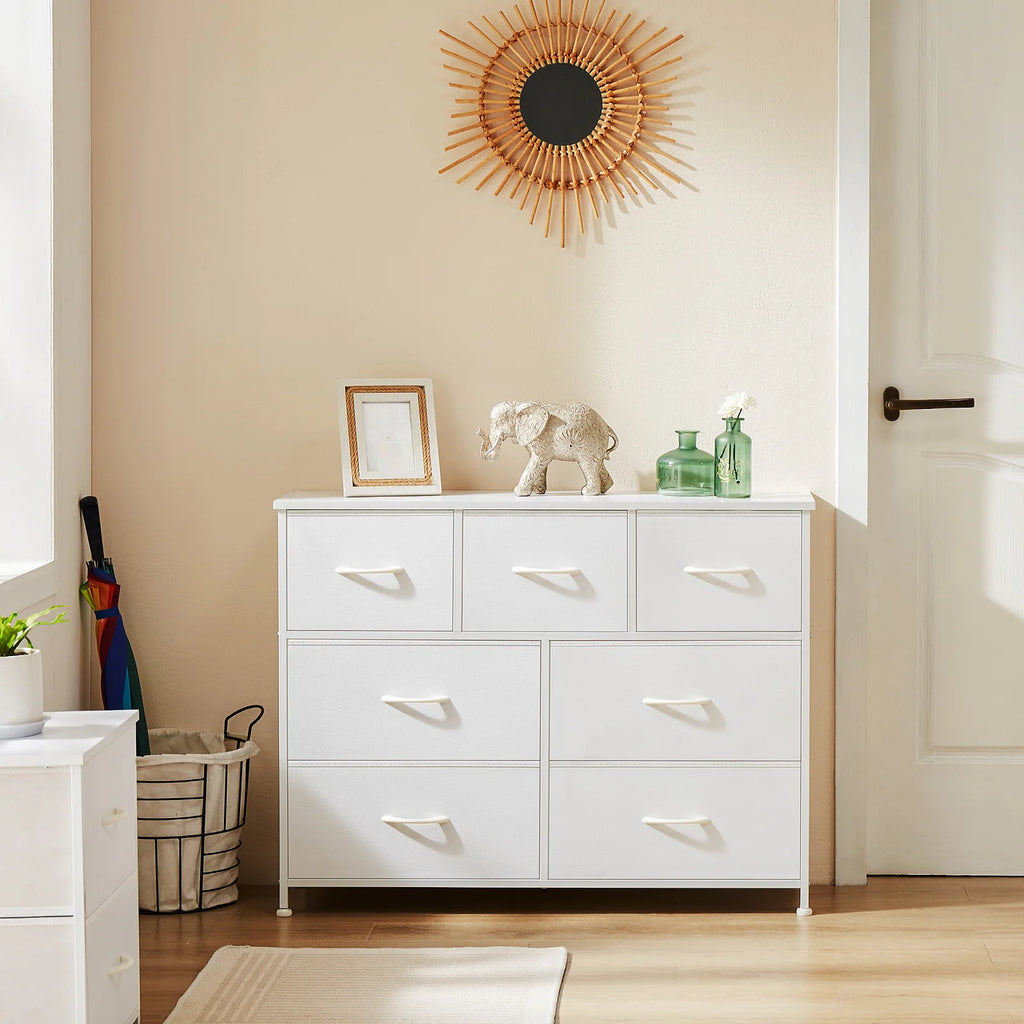 White dresser with decorative items in a room with a beige wall and wooden floor.