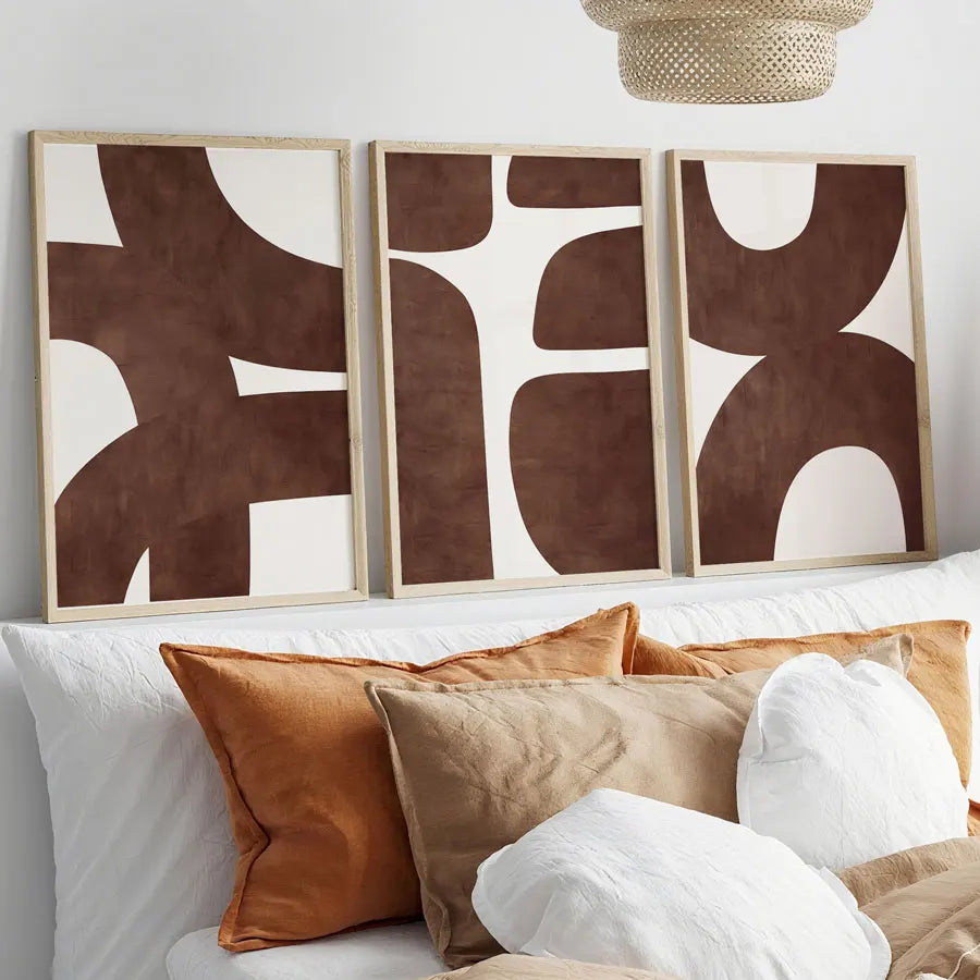 Three abstract art pieces on a wall above a sofa with colorful cushions.