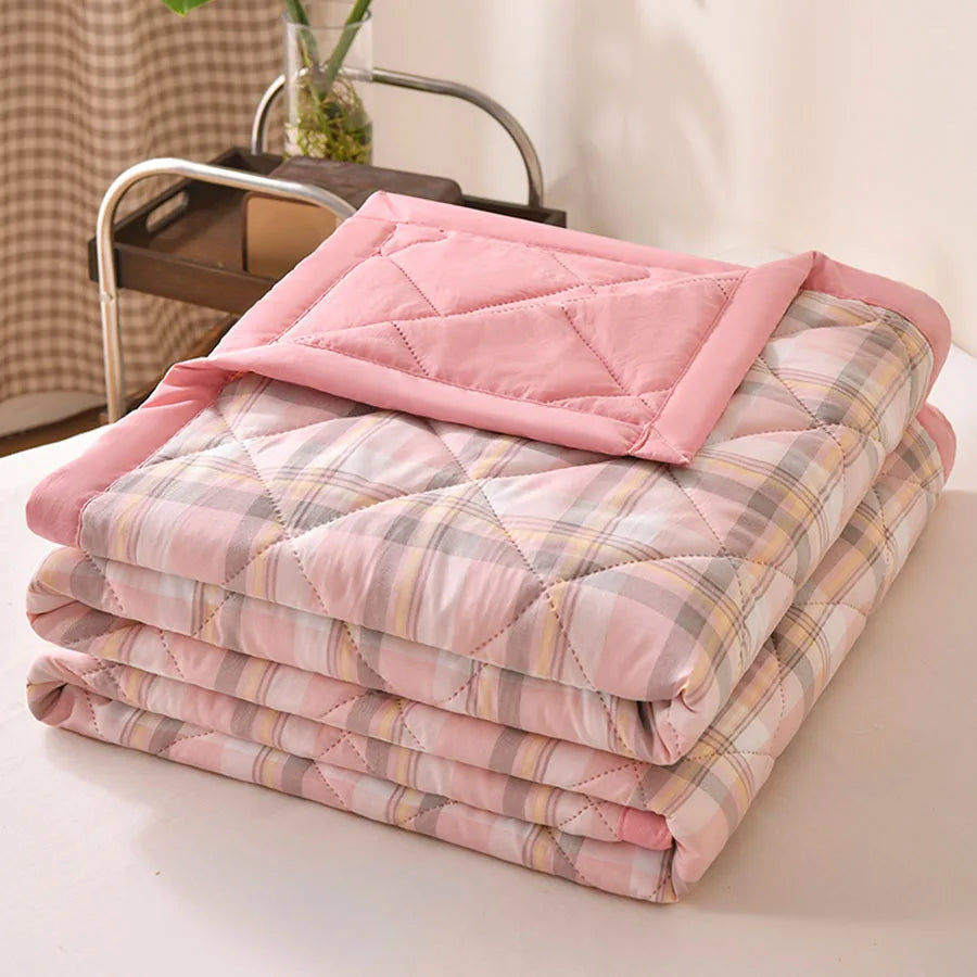 Blush pink plaid quilted comforter with grey and yellow lines and a pink border, folded on a bed