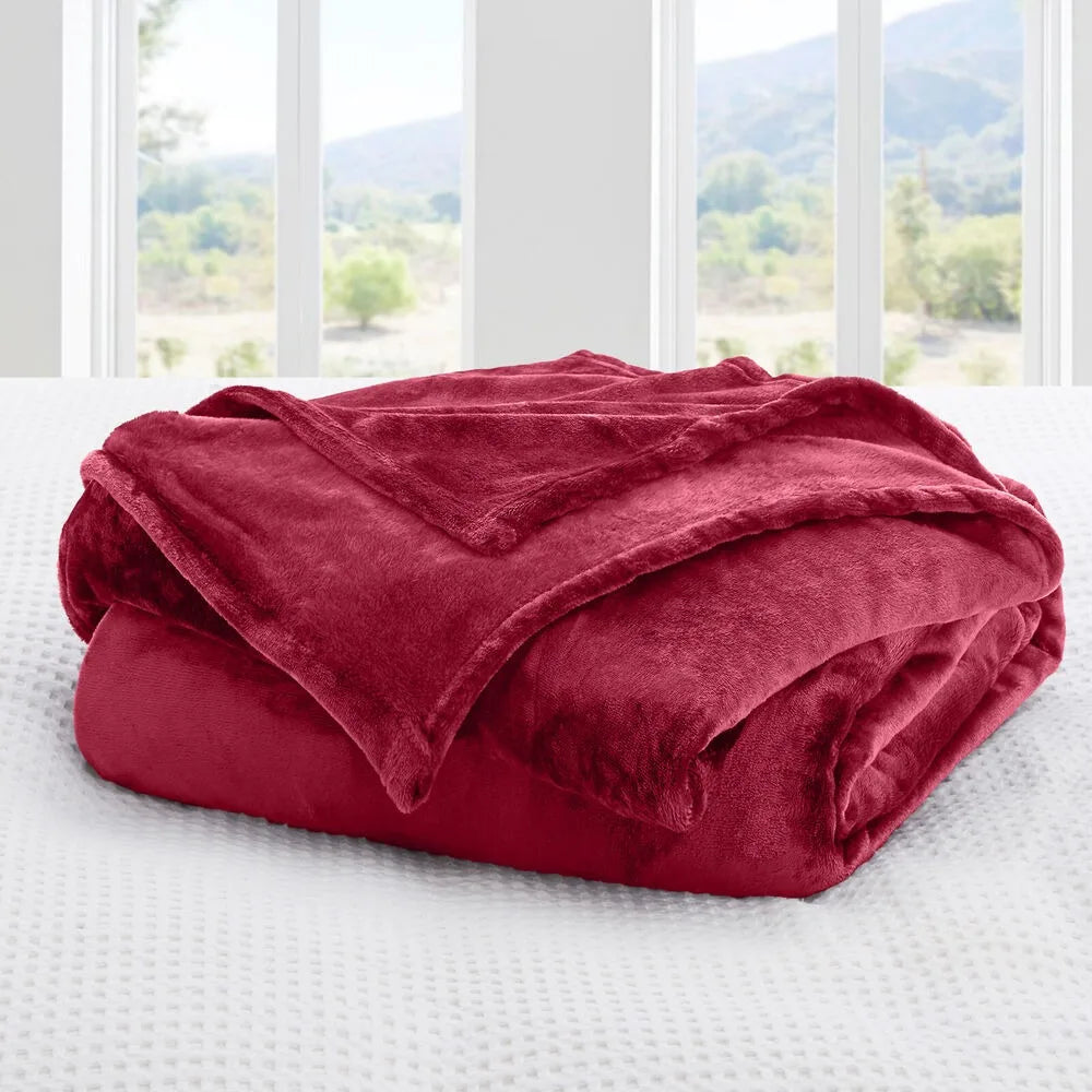 A wine red blanket on a bed with a window view of greenery
