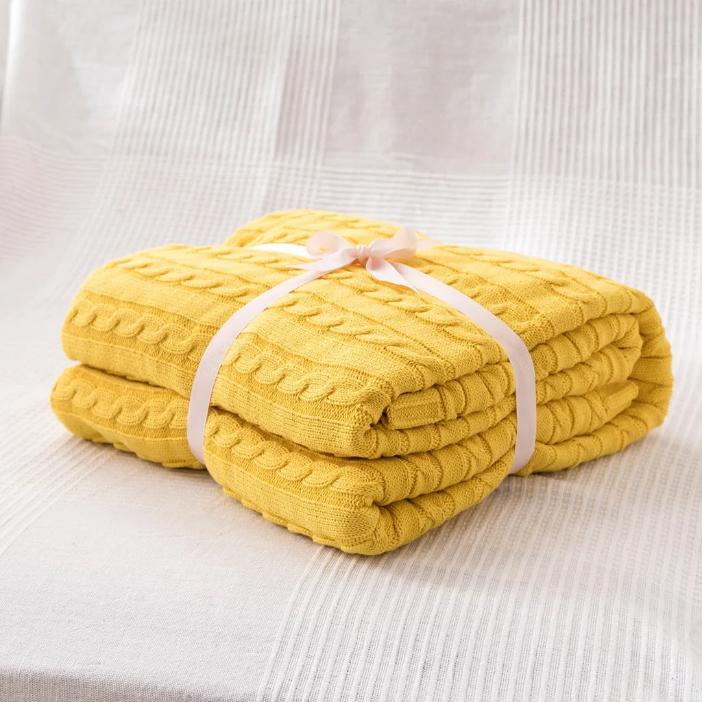 Yellow knitted blanket tied with a white ribbon on a light gray background
