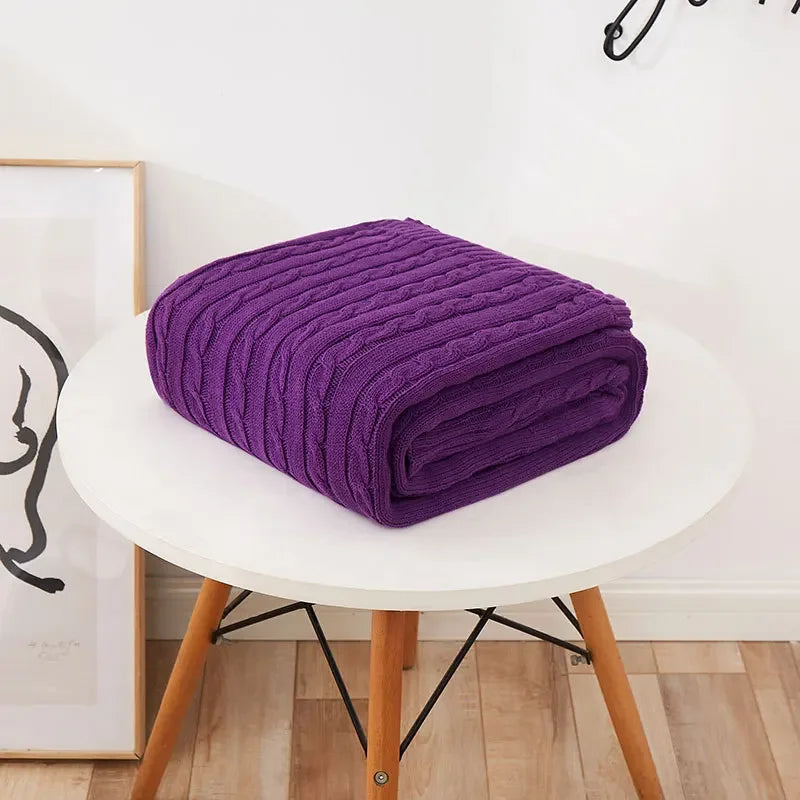 Folded purple blanket on a white chair with a light-colored wall and wooden floor in the background