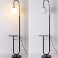 Black floor lamp with round glass shade and small table on a white background