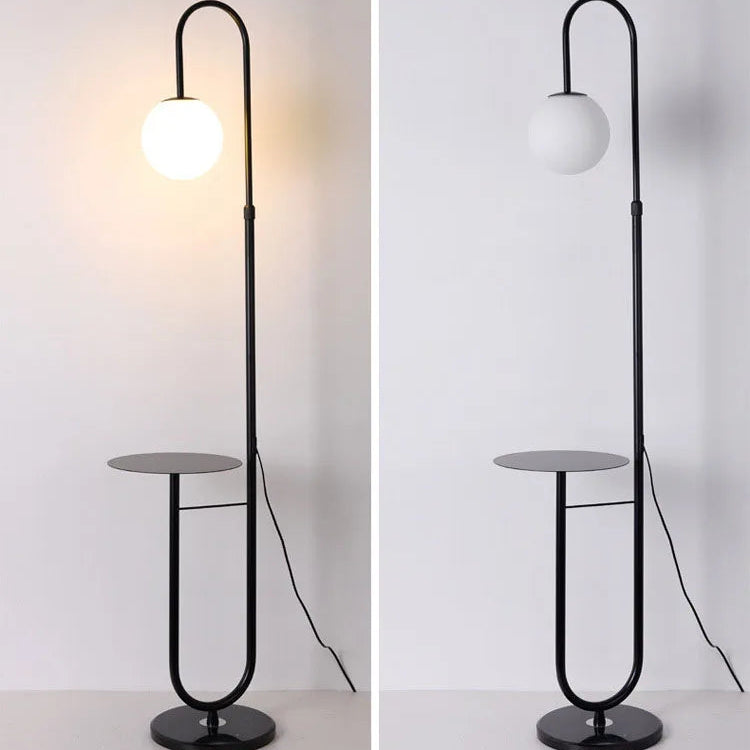 Black floor lamp with round glass shade and small table on a white background