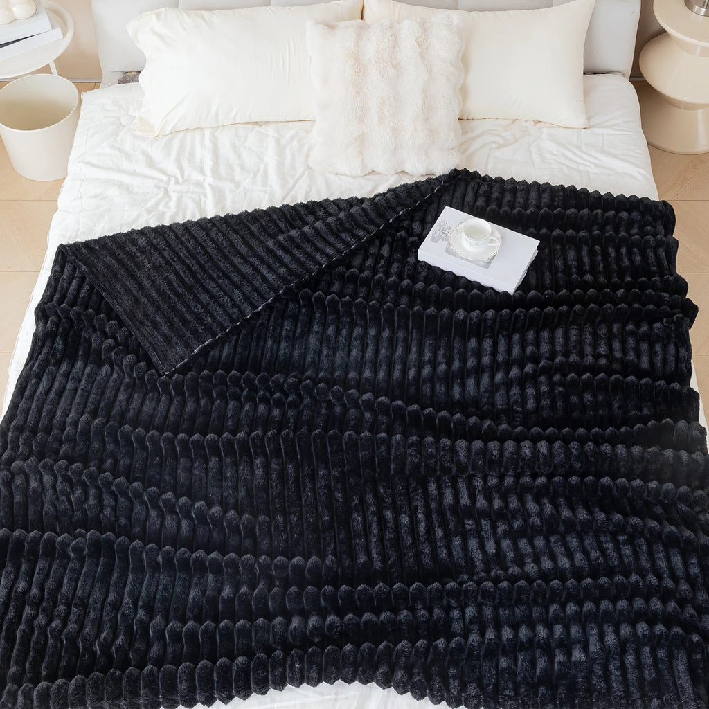 Black textured blanket draped over a bed with white bedding.