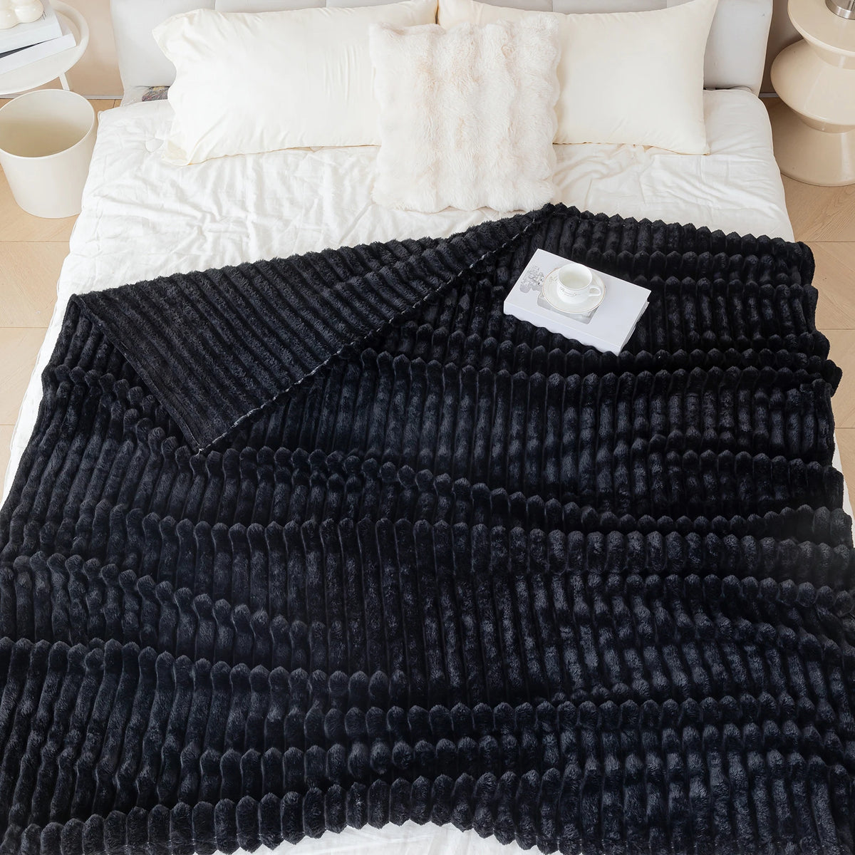 Black textured blanket draped over a bed with white bedding.