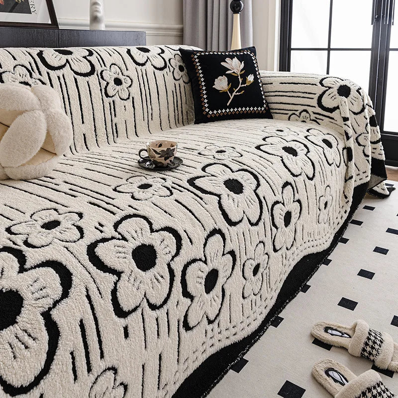 Cream and black floral-patterned sofa throw with bold contrast edging, neatly layered over a modern armchair sofa in a bright interior setting.