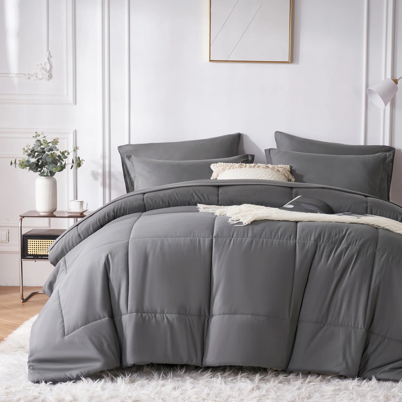 A grey comforter set on a bed in a bedroom with a white wall and decorative elements.