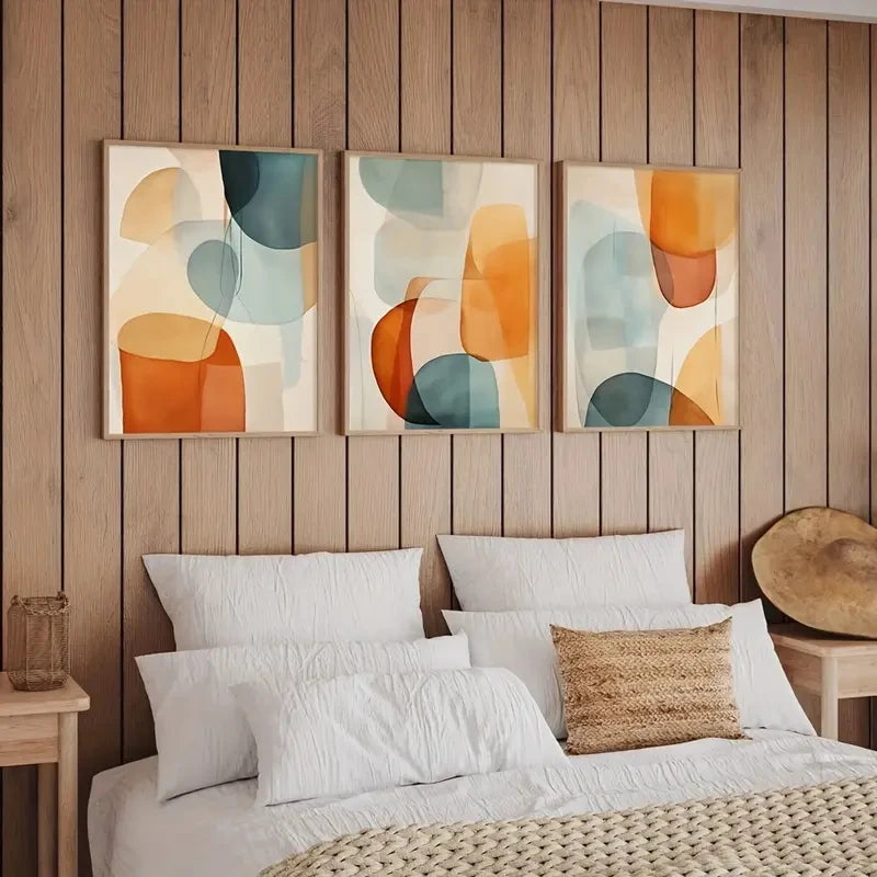Three abstract art pieces on a wooden wall above a bed with white bedding and a woven headboard.