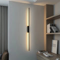 Vertical black line bar wall lamp casting warm light in a contemporary home study and living space