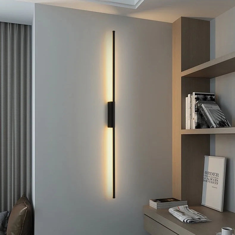 Vertical black line bar wall lamp casting warm light in a contemporary home study and living space