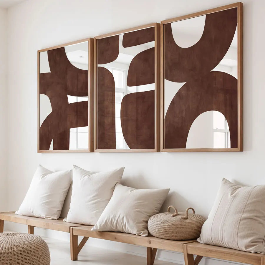 Abstract wall art in wooden frames above a bench with cushions in a minimalistic room.