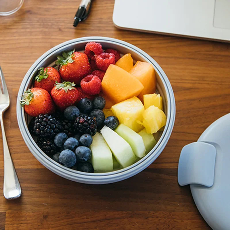 Fruit salad in a bowl on a wooden table with a fork and notebook.