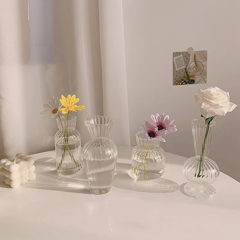Clear glass vases with flowers on a white surface against a neutral wall.