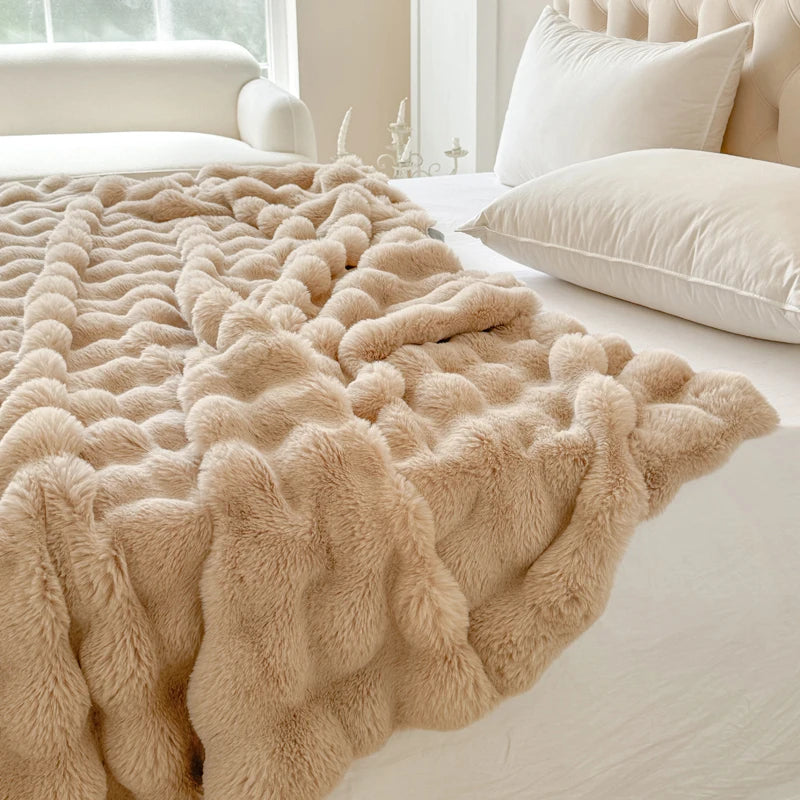 Beige fluffy blanket on a bed with white pillows and a neutral-colored headboard.