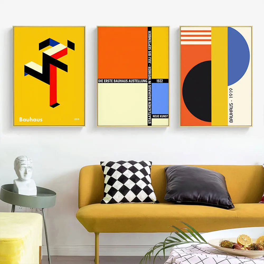 Three abstract art prints on a wall above a yellow sofa with decorative pillows.